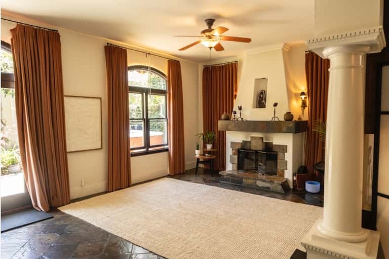 Residential living room with fireplace, brown curtains, ceiling fan, and French doors to patio