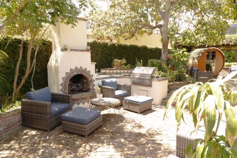 Backyard patio with wicker seating, pizza oven, built-in grill, and lush garden landscaping