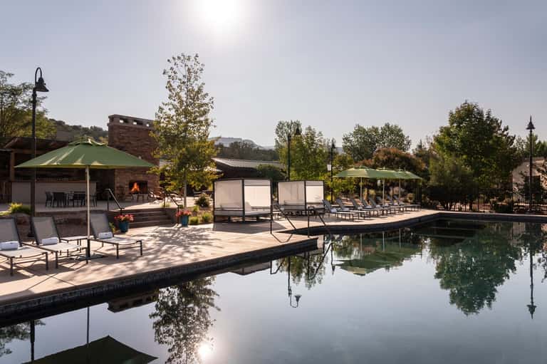 Lakeside resort pool area with stone fireplace, lounge chairs, and tree-lined surroundings