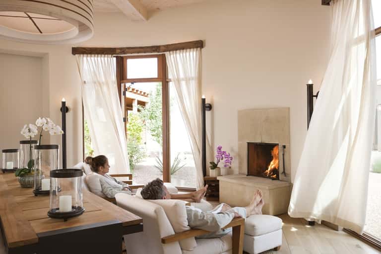 Spa relaxation room with fireplace, cream seating, flowing white curtains, and ocean view doors