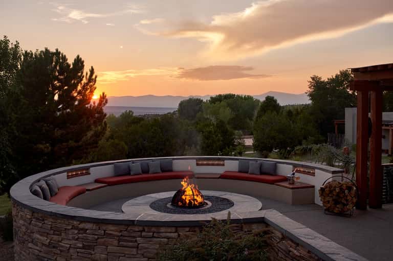 Circular fire pit seating area with built-in bench, mountain sunset views, and evening lighting