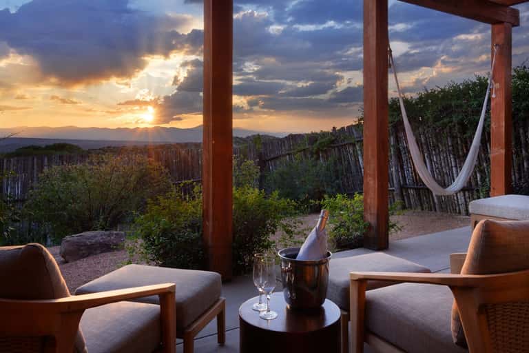 Desert sunset view from covered patio with wooden posts, comfortable seating, and wine service