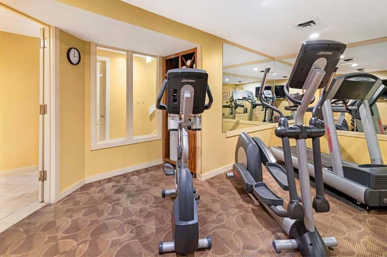 Fitness center with cardio equipment, mirrors, yellow walls, and modern exercise machines