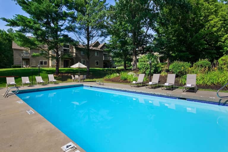 Resort outdoor swimming pool surrounded by lounge chairs, trees, and residential buildings on lawn