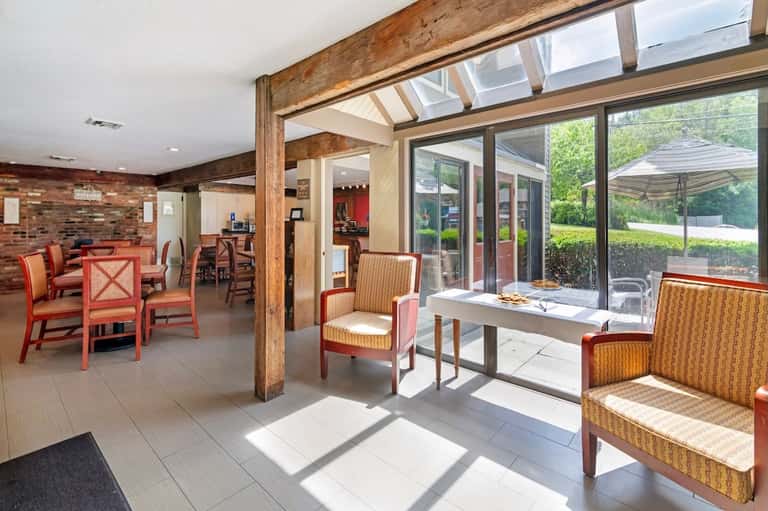 Bright sunroom with brick fireplace, red chairs, large windows, wood beams, and outdoor patio access