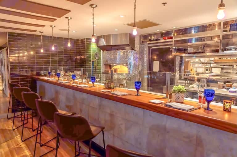 Modern hotel bar with wooden counter, pendant lighting, and stocked shelves