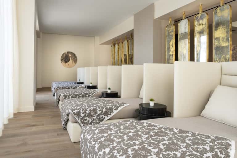 Luxury spa or wellness room with multiple single beds and gold-framed mirrors
