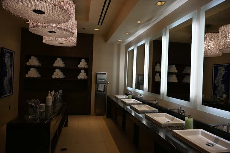 Luxury bathroom with multiple sinks, lighted mirrors, and decorative towel storage