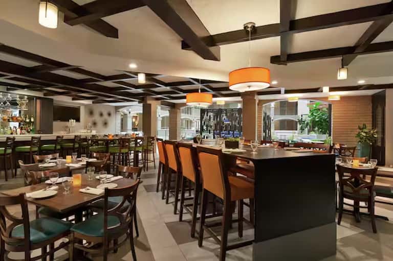 Modern restaurant interior with wooden tables, orange pendant lights, and bar seating