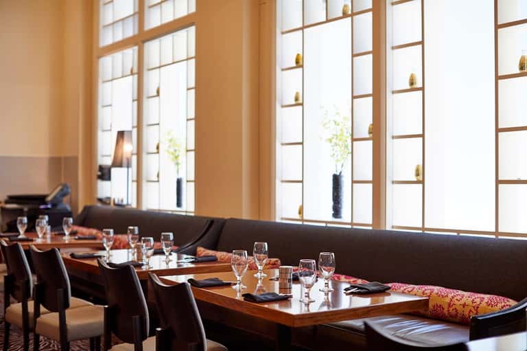 Upscale restaurant dining room with wooden tables, dark chairs, and floor-to-ceiling windows