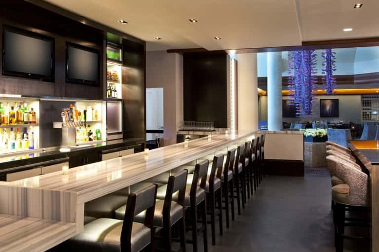 Upscale bar interior with light wood counter, black seating, and ambient lighting