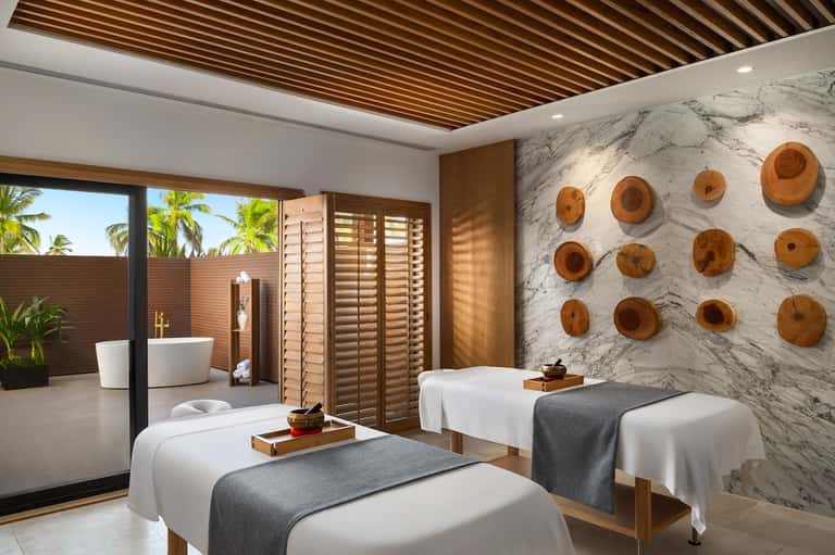 Luxury spa treatment room with marble walls, wooden accents, and outdoor soaking tub