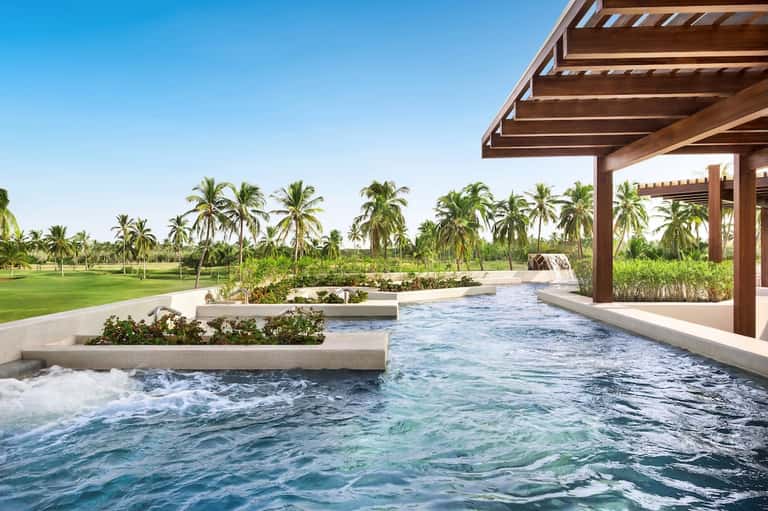 Infinity pool overlooking tropical golf course landscape with wooden pergola