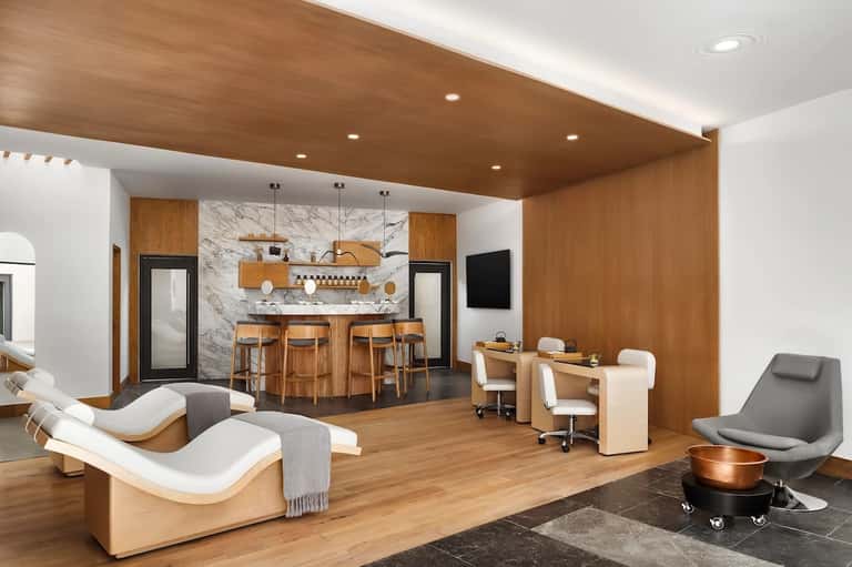 Modern luxury spa lounge with wooden beams, marble accents, comfortable seating, bar area, and warm ambient lighting