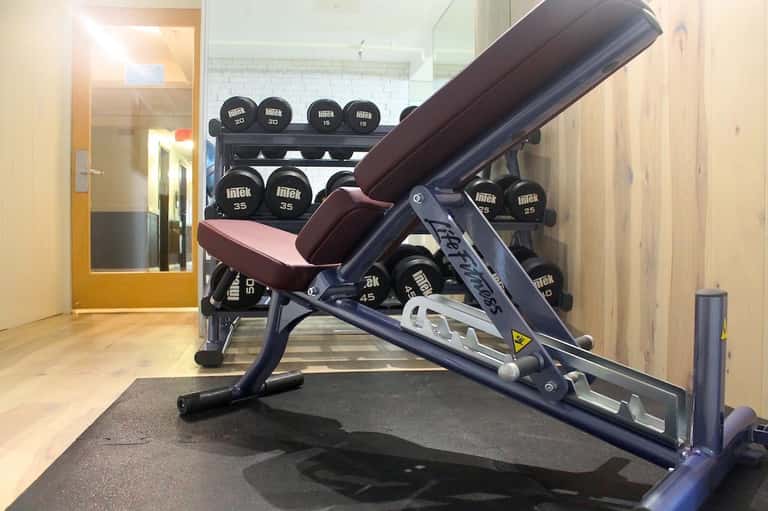 Fitness center featuring weight bench and dumbbell rack with mirrors and wooden flooring