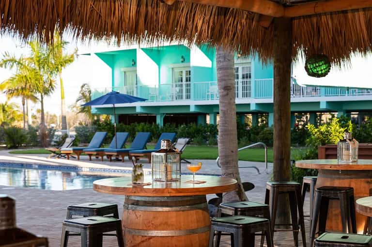 Turquoise tropical home with pool, lounge chairs, thatched bar structure, and manicured lawn