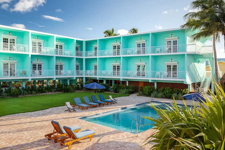 Turquoise hotel building with white railings, pool deck with lounge chairs and blue umbrellas