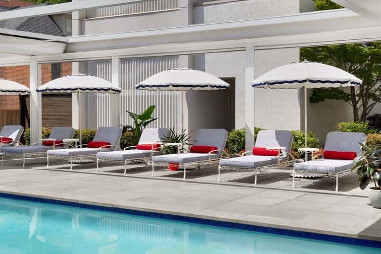 Poolside lounge area with striped chaise lounges, white scalloped umbrellas, and green landscaping