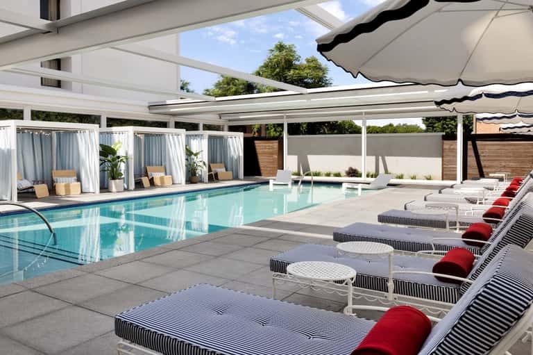 Indoor pool with retractable roof, white umbrellas, loungers with red cushions, and curtained cabanas