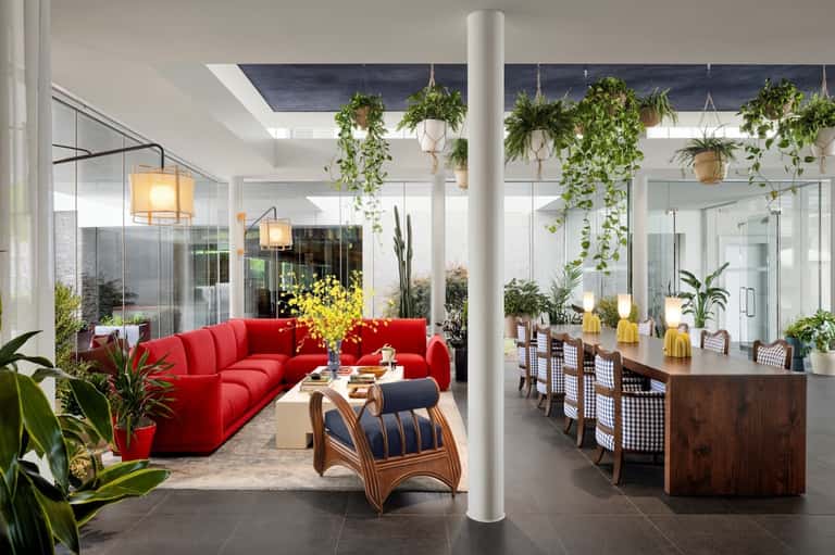Contemporary hotel lobby with red sofa, plants, wooden bar, and bright atrium