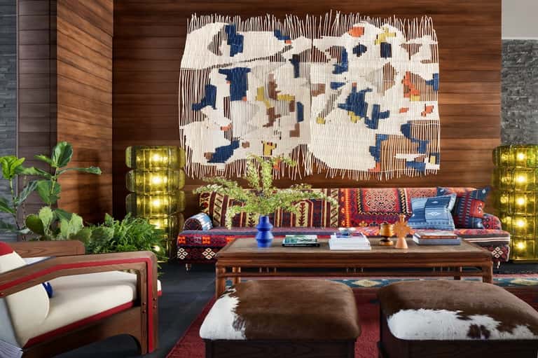Modern lobby lounge with wooden wall art, colorful patterned seating, brass planters, and contemporary decor