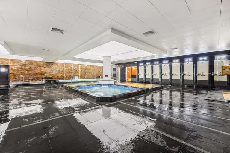 Modern indoor swimming pool with sleek design, skylights, spa area, and mirrored glass walls