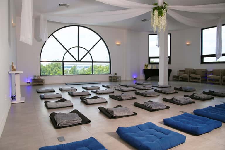 Meditation or yoga studio with arched windows, rolled yoga mats on floor, blue cushions, and scenic landscape view