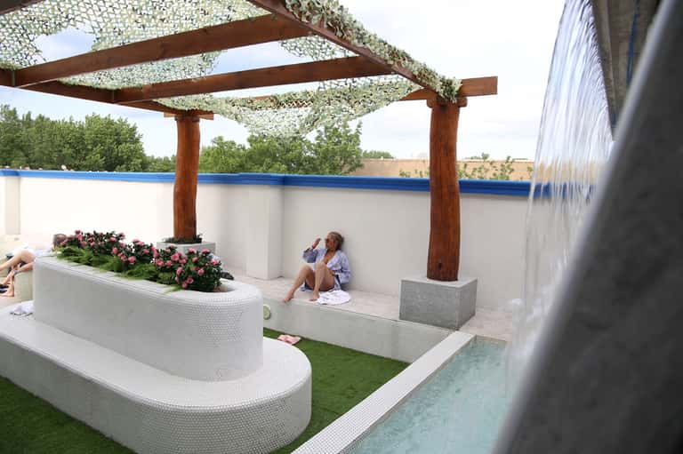 Poolside lounge area with modern seating, pergola shade, and water feature
