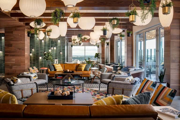 Modern hotel lounge with hanging pendant lights, wood ceiling, colorful seating, and floor-to-ceiling windows