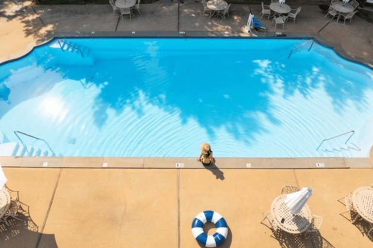 Overhead view of swimming pool with person standing on deck, umbrellas, and lounge chairs casting shadows