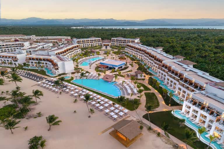 Aerial view of large beachfront resort complex with multiple pools and surrounding forest