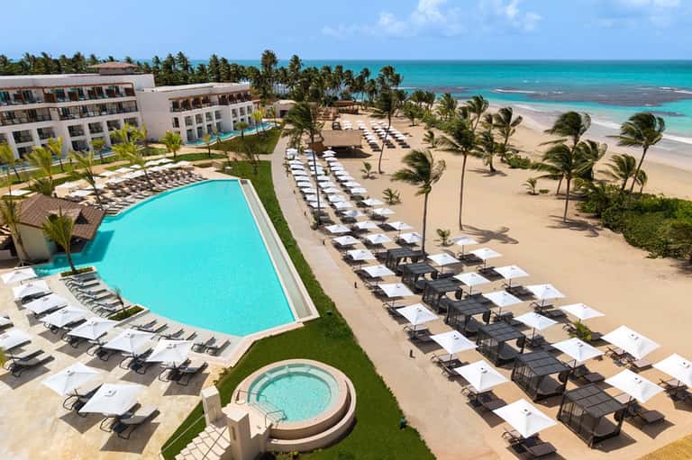 Beachfront resort with pool, lounge chairs, palm trees, sandy beach, and turquoise ocean view