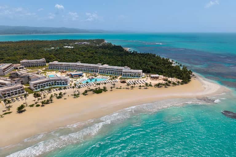 Aerial view of beachfront resort with curved pool, private beach, and tropical surroundings
