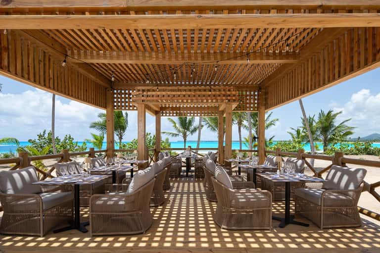 Beachfront wooden pergola restaurant with ocean view, striped seating, and tropical setting
