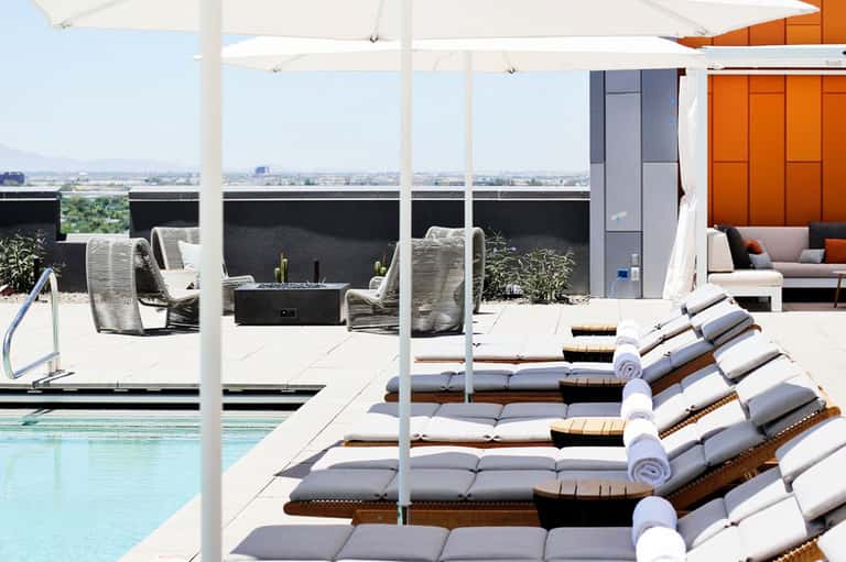 Rooftop pool area with lounge chairs, white umbrellas, and panoramic city views