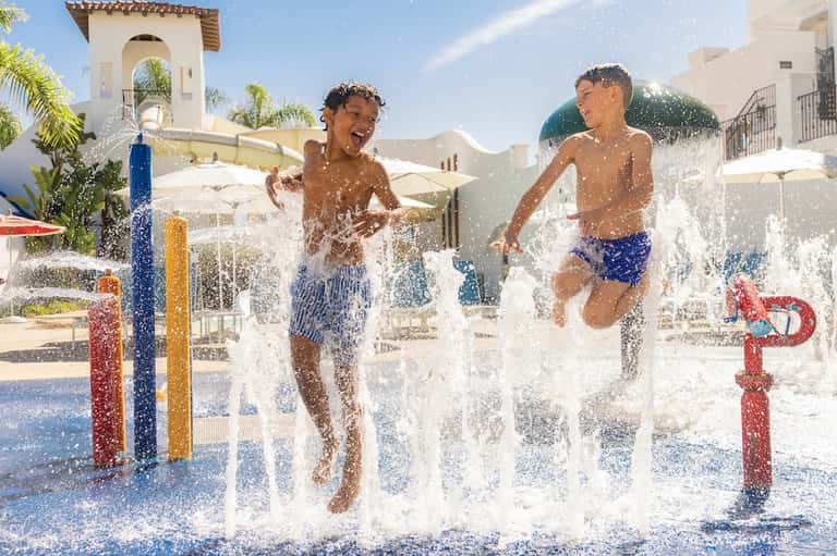 Children playing in splash pad with water fountains at resort courtyard with Spanish architecture