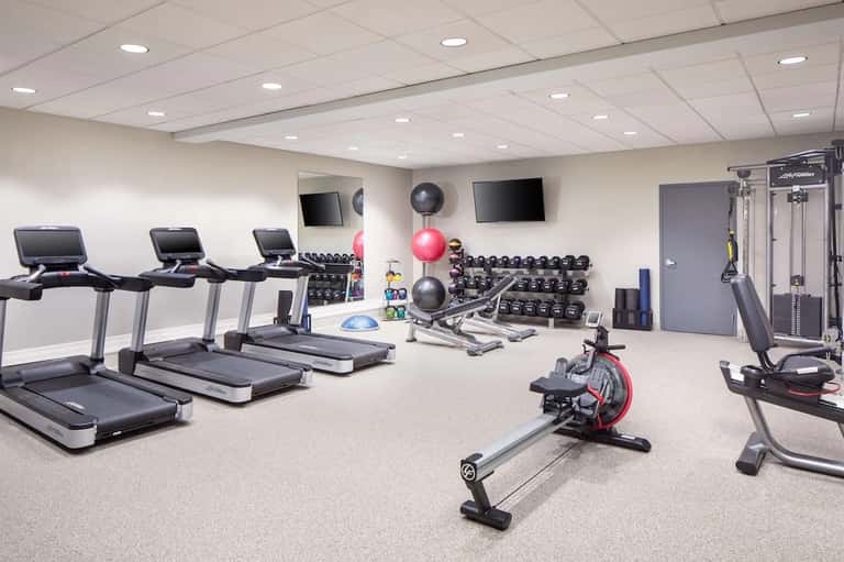 Modern fitness center with treadmills, dumbbells, exercise bikes, and TV screens