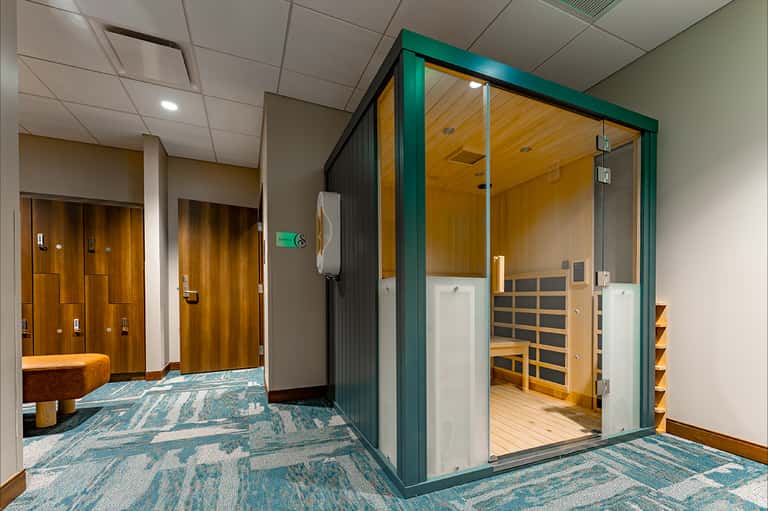 Spa room entrance with green frame door, sauna visible inside, wood paneling, and patterned carpet
