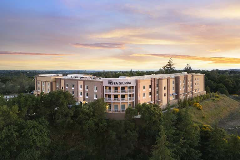 Vista Sierra hotel building at dusk with illuminated facade nestled among green hillside trees