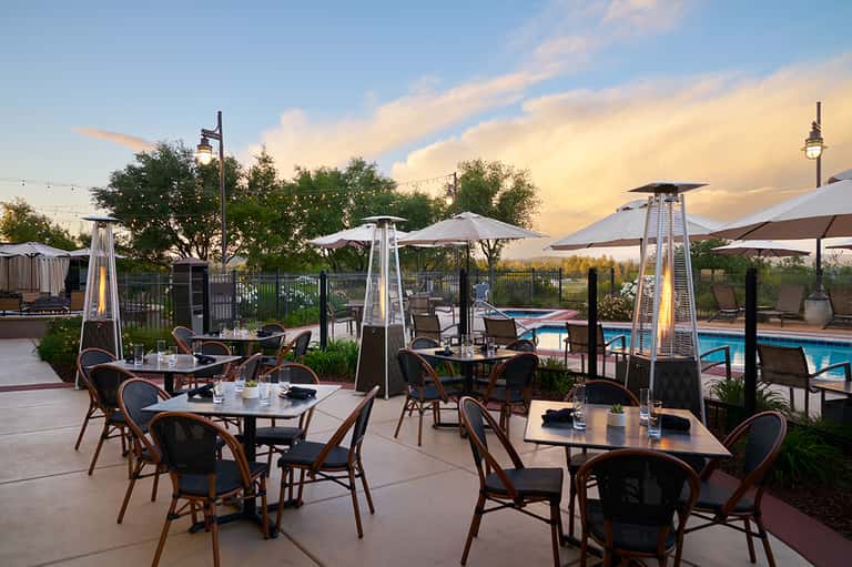 Poolside dining area with heat lamps, umbrellas, tables at sunset