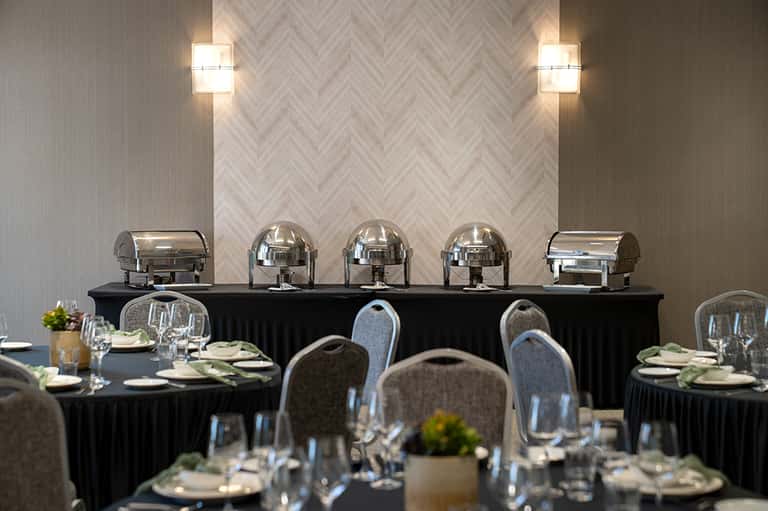 Formal banquet room with round black tables, place settings, and silver chafing dishes