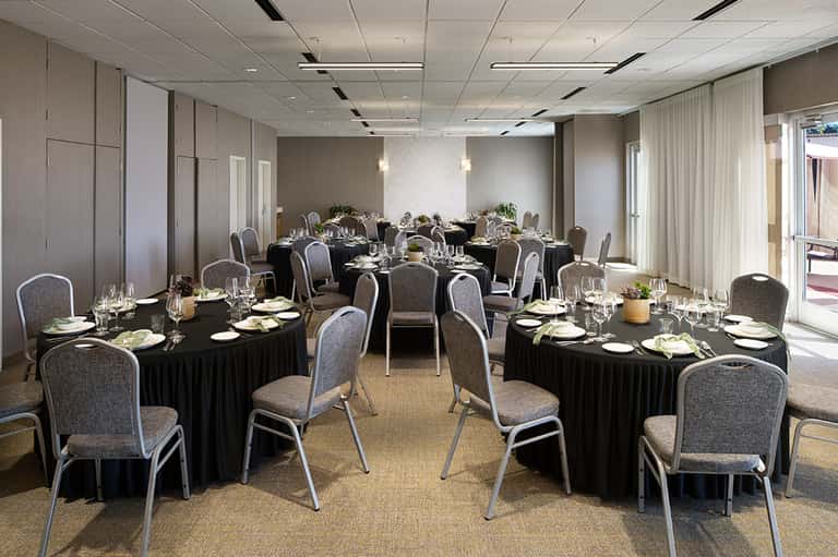 Elegant ballroom with round tables set with black linens, gray chairs, and natural light from floor-to-ceiling windows