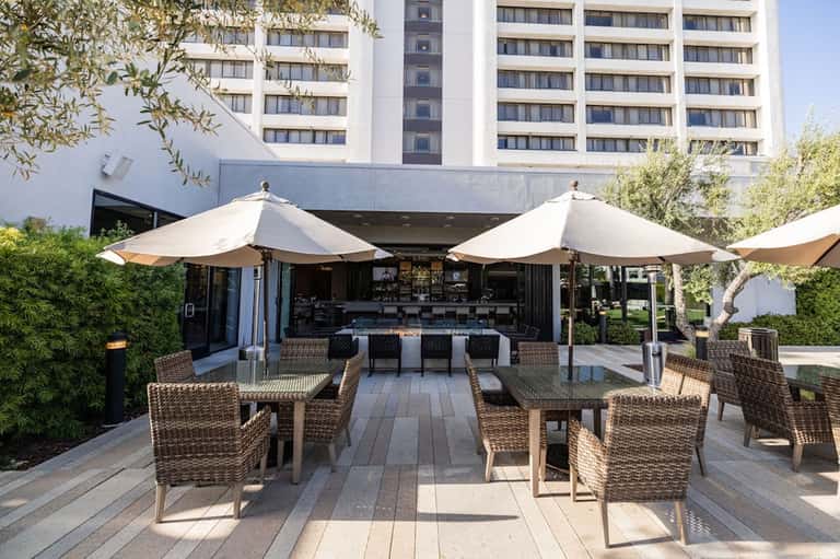 Contemporary outdoor patio with cream umbrellas, rattan chairs, wooden deck, and modern building