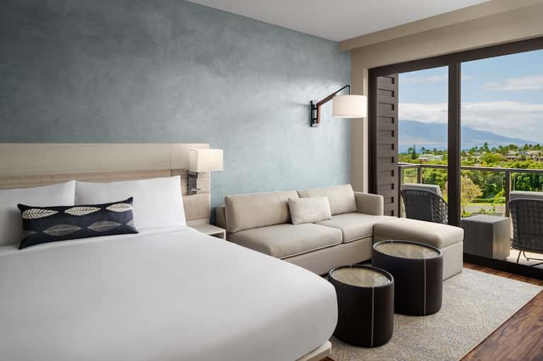 Modern hotel room with bed, sofa, mountain view balcony, and contemporary minimalist design