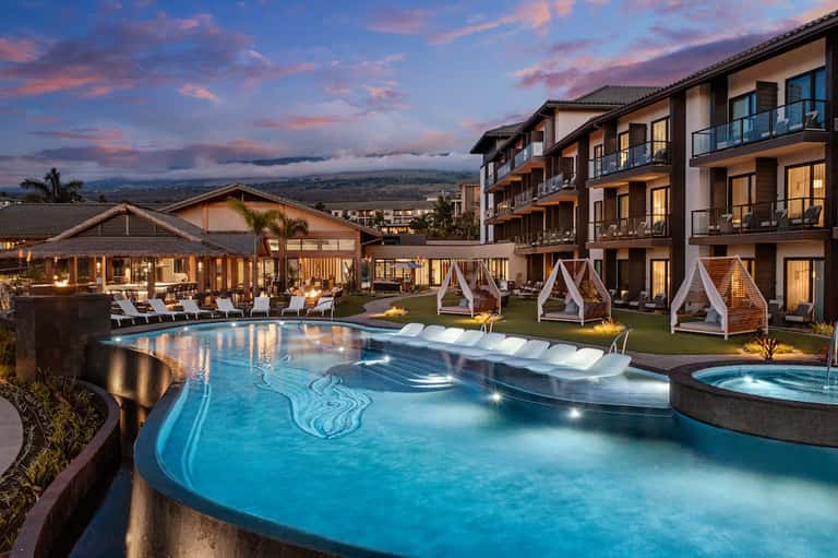 Resort pool complex at sunset with white cabanas, lounge chairs, and mountain valley views