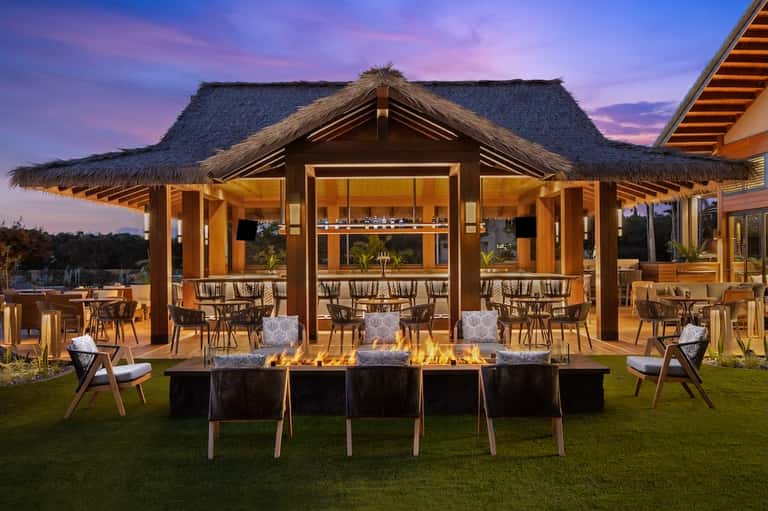 Luxury outdoor pavilion with thatched roof, fire pit, and lounge seating at dusk