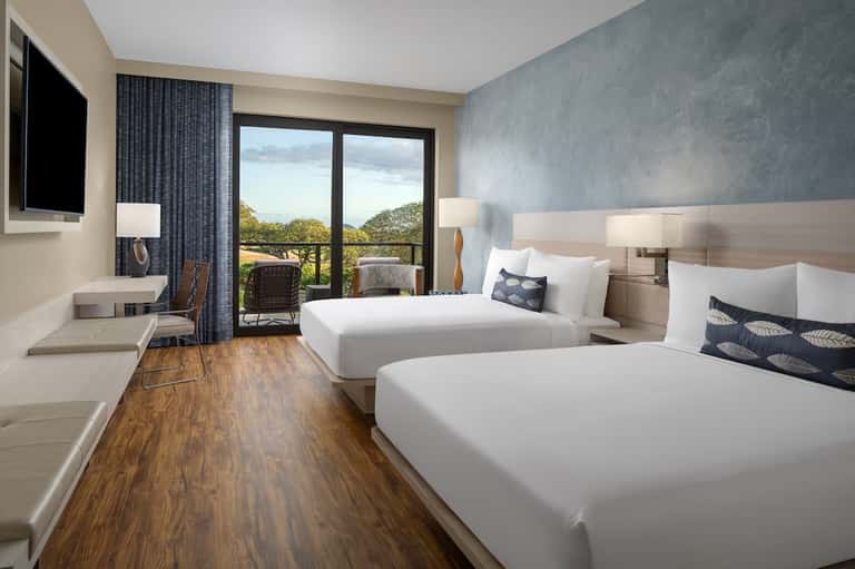 Hotel room with two queen beds, wooden flooring, balcony doors, and nature landscape views
