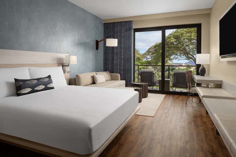 Hotel bedroom with queen bed, blue accent wall, balcony doors, and nature views