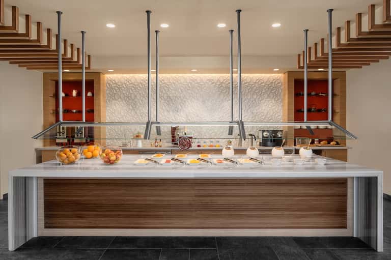 Upscale hotel buffet counter with white marble top, wood accents, and fresh fruit displays