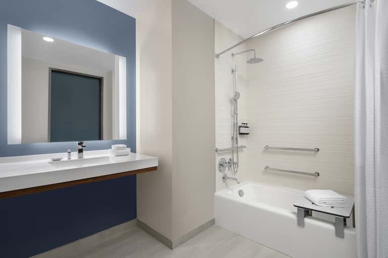 Modern bathroom with illuminated mirror, dark vanity, white tile, and walk-in shower area